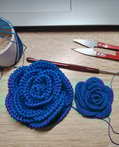 rose faite au crochet dans un fil fin de couleur bleu posé sur une table un crochet et un ciseaux
