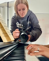 A young female filmmaker is filming a close-up of a piano players fingers as he plays a song.