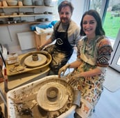 a man and woman are smiling and having fun in the pottery on the 2hr throwing workshop