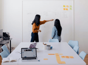 two women standing in front of a white board board
