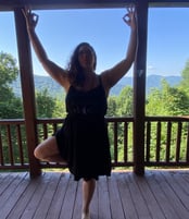 Rachel on balcony doing yoga with mountain range and tall trees and background