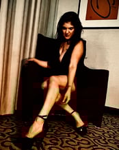 Coralyn wearing black dress posing on recliner chair.