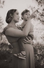 Pregnant mom holding toddler, both pointing and looking into the distance.