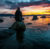 a man sitting on a rock in the water watching the sunrise