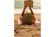 A woman on the beach lies on her back and reads a book