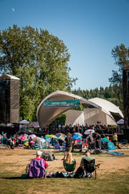 Spectators seated on recliners in a park, listening to the choir from an outdoor concert stage