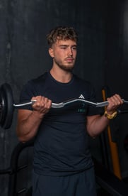 Antrenor personal executând flexii pentru biceps cu o bară EZ, într-o sală de fitness