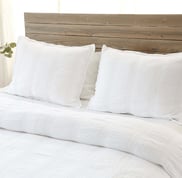 a bed with white linens quilt and pillows on top of a wooden headboard