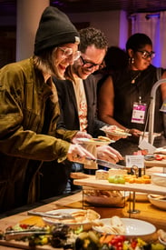 Guests at a VIFF reception laughing while filling their plates from an enticing buffet full of food