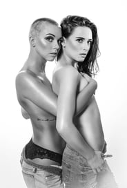Schwarz-Weiß-Porträt von zwei Frauen, die sich umarmen, eine mit Kurzhaarfrisur und Tattoo.