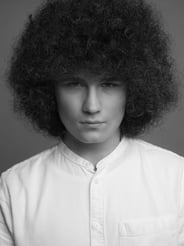 Schwarz-Weiß-Porträt eines jungen Mannes mit voluminösem Afrohaar und weißem Hemd.