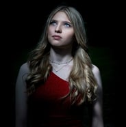 Porträt einer blonden Frau mit blauen Augen, die ein rotes, glitzerndes Kleid trägt und nach oben schaut.