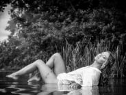 Schwarz-Weiß-Aufnahme einer Frau in einem nassen Hemd, die entspannt im Wasser liegt.