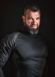 Porträt eines muskulösen Mannes mit Bart und Seitenhaarschnitt in einem schwarzen Rollkragenpullover.