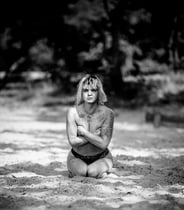 Schwarz-Weiß-Aufnahme einer tätowierten Frau mit kurzen Haaren, die im Sand kniet.