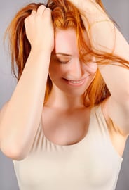 Porträt einer lächelnden Frau mit roten Haaren, die die Hände in ihren Haaren hält.