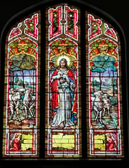 A stained glass window featuring Jesus and several sheep, Jesus holds a lamb in his arms