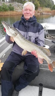 a man is sitting in a fishing boat in sweden, he caught a pike in sweden.