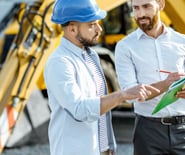 two men in hard hats and hard hats standing in front of a construction site