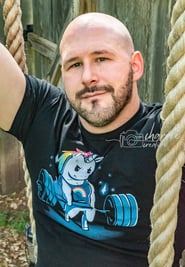 young bald, bearded man on rope swing with weight-lifting rainbow unicorn on shirt