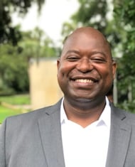 Dollar Harmony Coach Wildo in a suit and white shirt smiling
