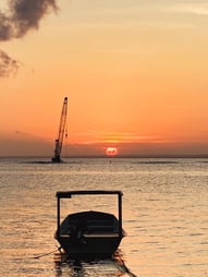 Coucher de soleil sur la plage de Nusa Lembongan avec un bateau en premier plan et la grue au large près du spot de surf.
