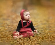 a baby girl sitting on a leaf covered ground