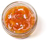 Top-down view of a little, clear, open container of orange mango chutney Chutneys