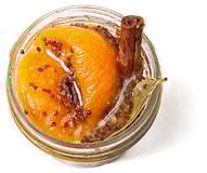 Top down view of a little, clear, open container of peach mostarda with mustard seeds & a bay leaf.