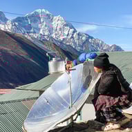 Femme népalaise chauffant de l'eau avec un panneau solaire, au cœur des montagnes enneigées de l'Himalaya.