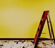 intérieur avec un mur jaune, avec un escabot en bois marron, ave du papier journal au sol 