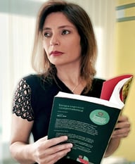 Psicóloga Dayane Machado Terapia Cognitiva Comportamental tcc olhando para o lado pensativa segurando um livro