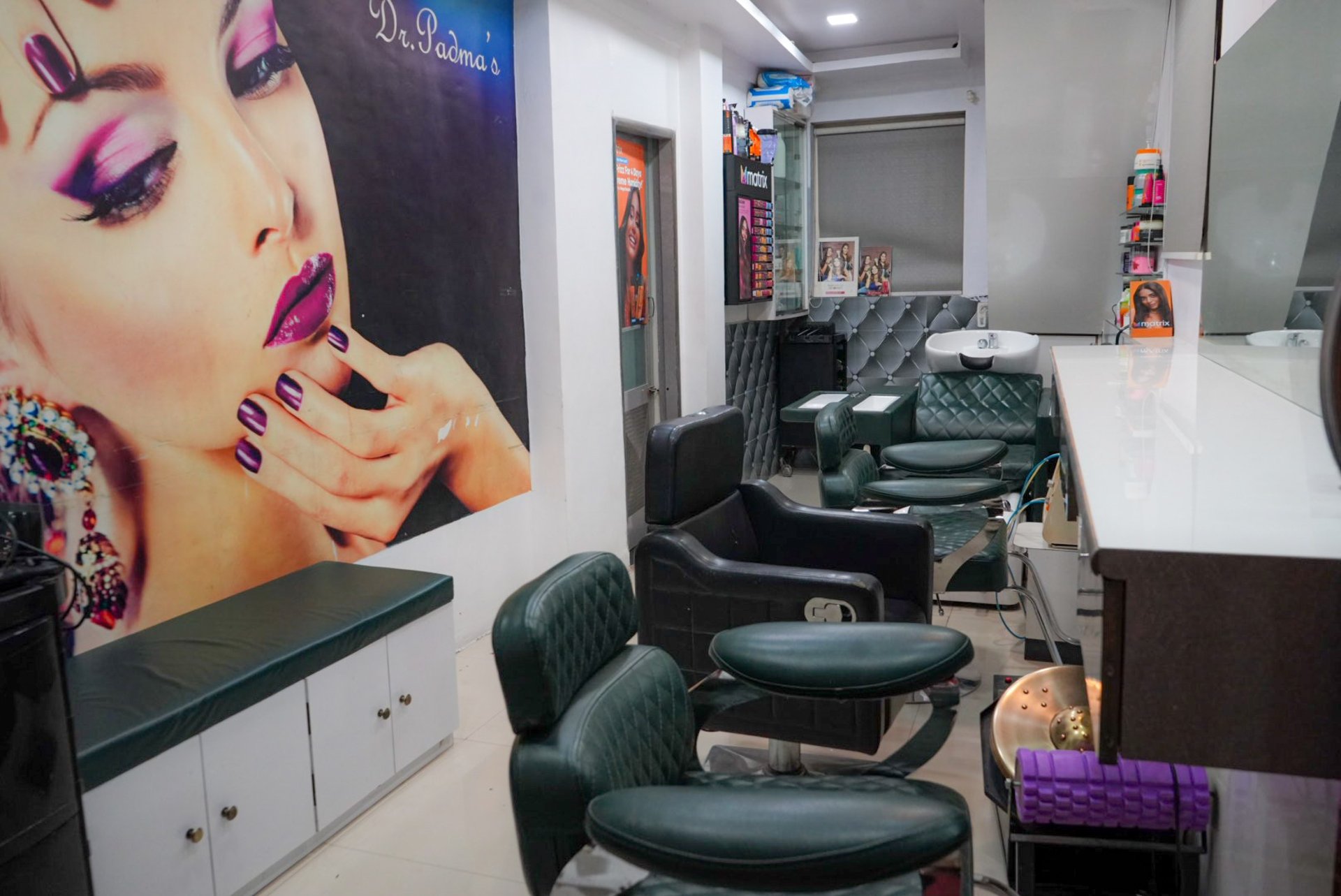 grayscale photo of woman using laptop near three salon chairs