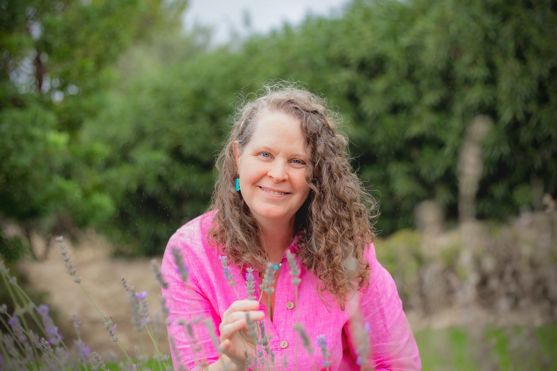Sheila Doerfler in magenta blouse holding lavender in her fingers and smiling