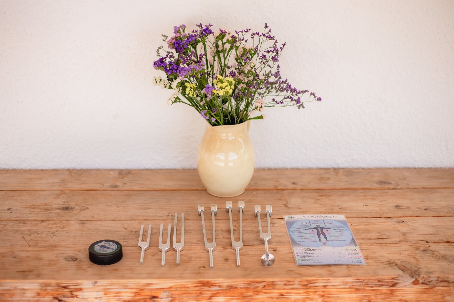 Spanish still life of 6 tuning forks on a rustic wood table with a cream ceramic pitcher filled with wild flowers