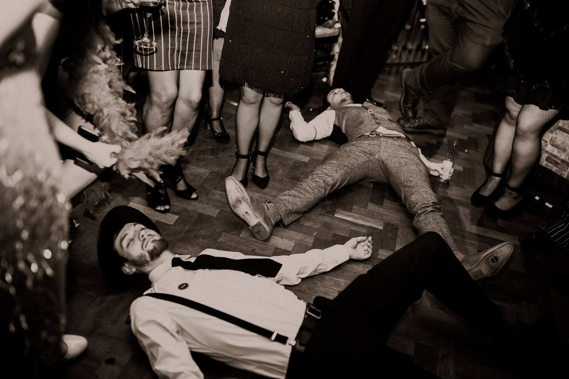 two men lie down on the floor at a 1920s themed murder mystery party.