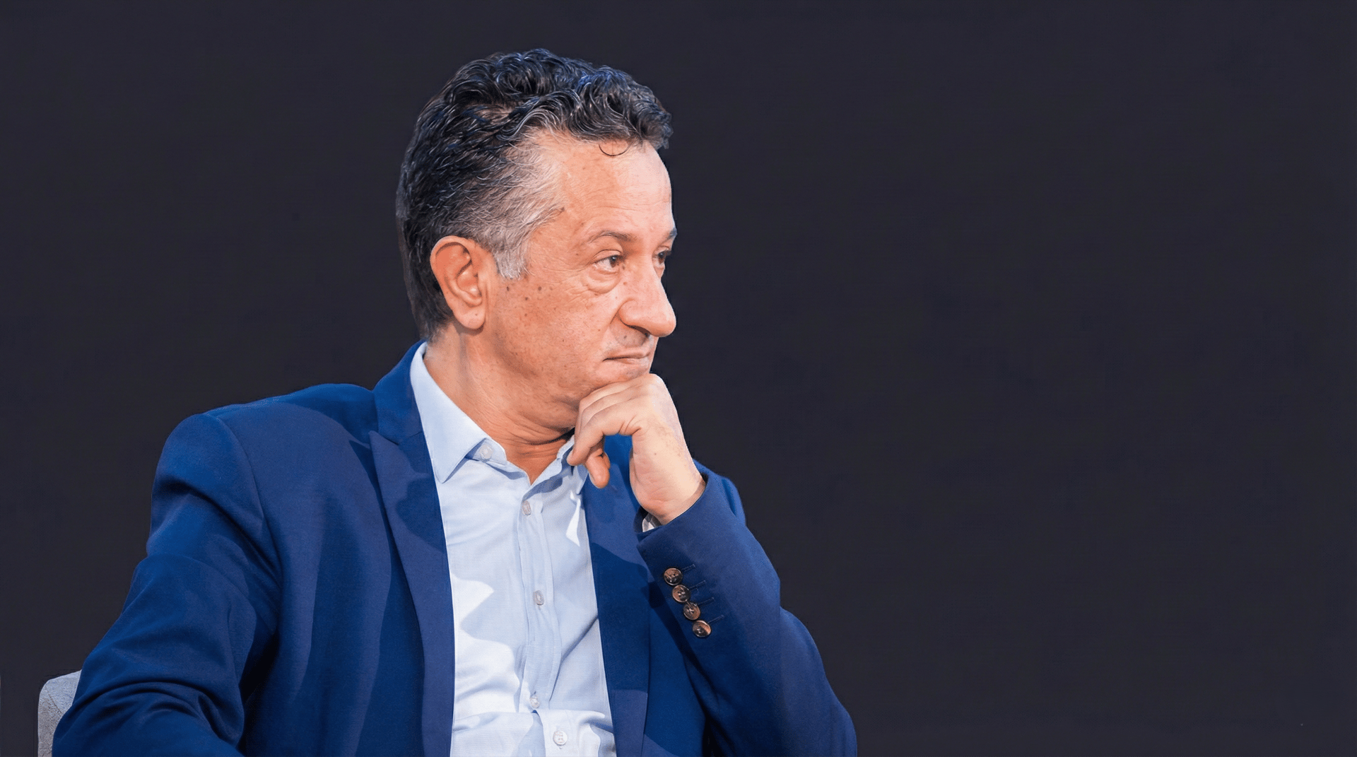 Mohammed Baida, an expert in media and corporate communication, seated in contemplation wearing a formal suit.