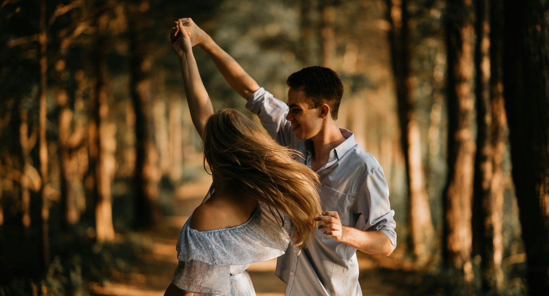 A happy couple holding hands up in the air in a park.