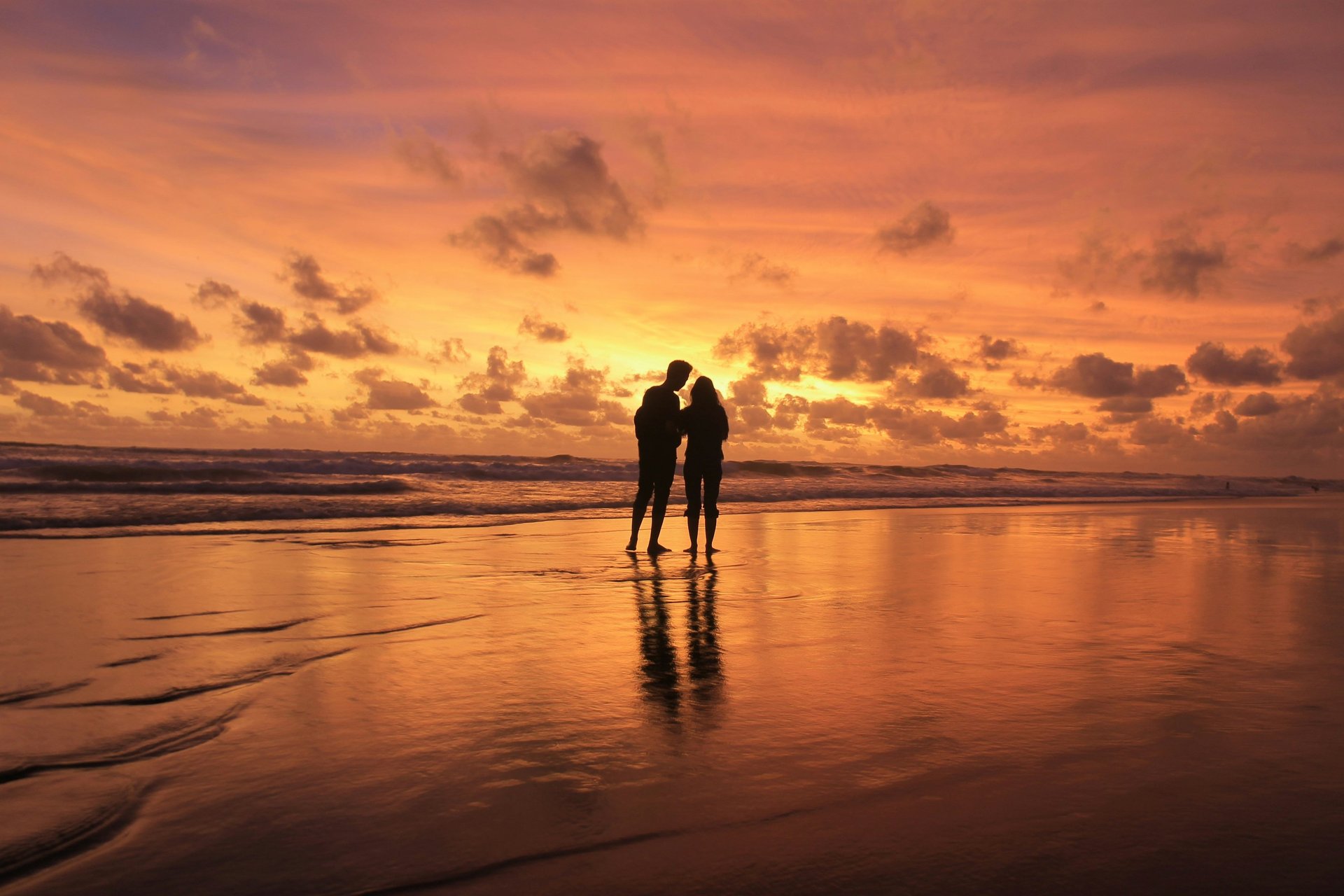 A couple standing on the shore of the sea, watching a gorgeous sunset.