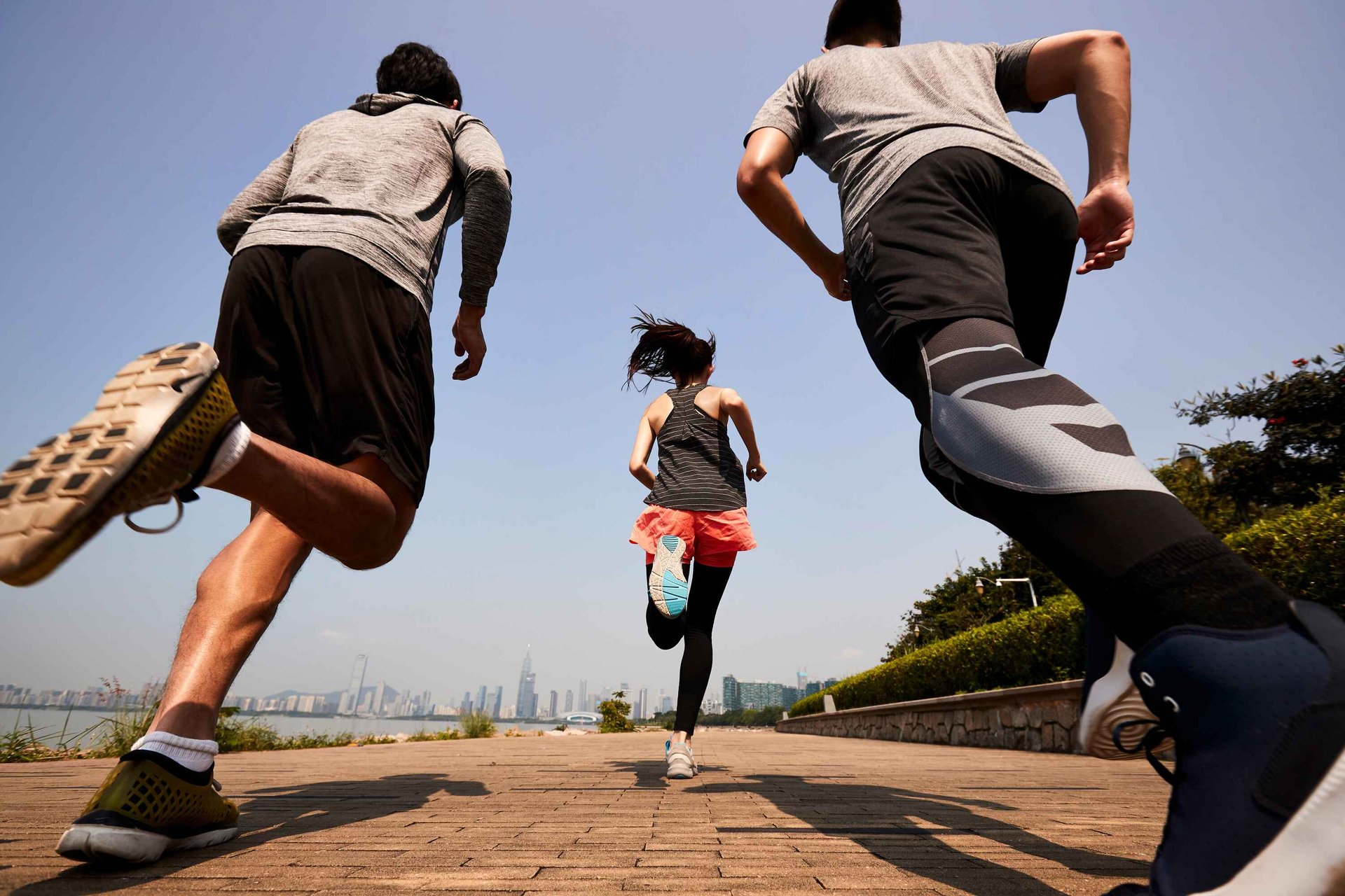 The back of 2 men and 1 woman running along the Hong Kong harbour