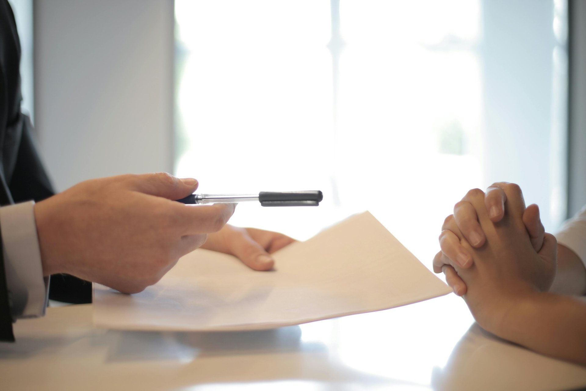 woman signing on white printer paper beside woman about to touch the documents