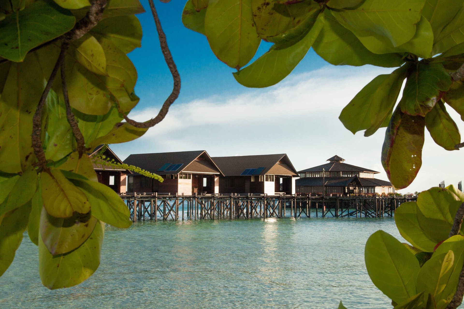 View of a water chalet and the main building, framed by tropical foliage.