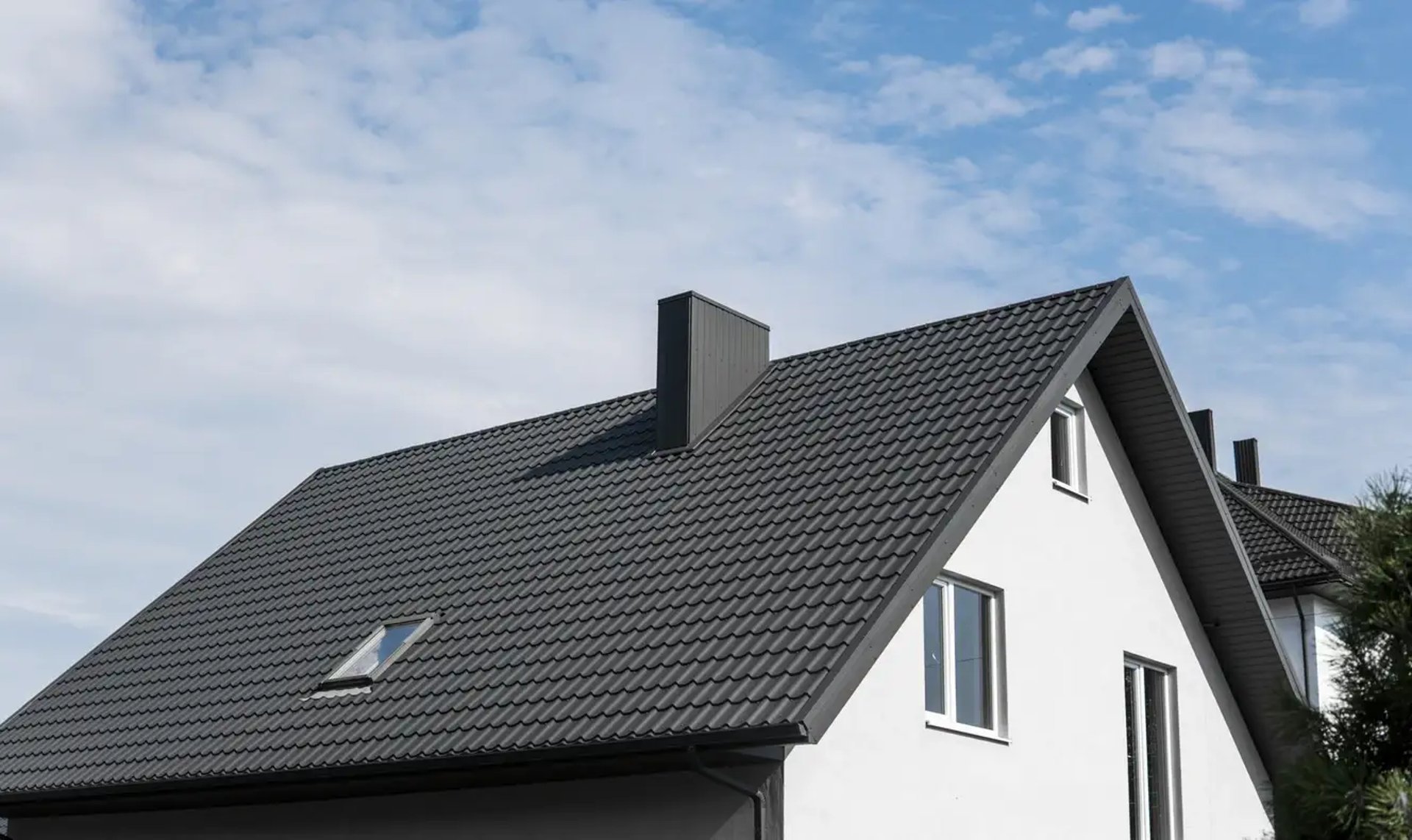 Custom home with a white stucco facade and a black shingle roof against blue sky.