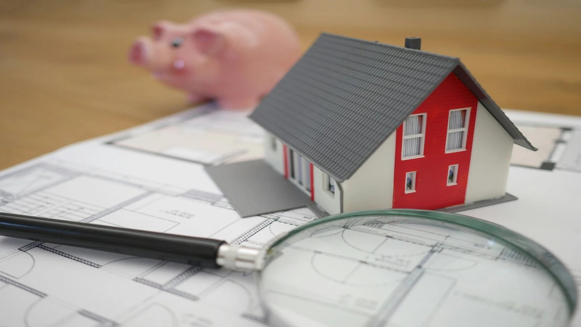 House model placed on architectural blueprints with a magnifying glass and pen, representing property planning and valuation.
