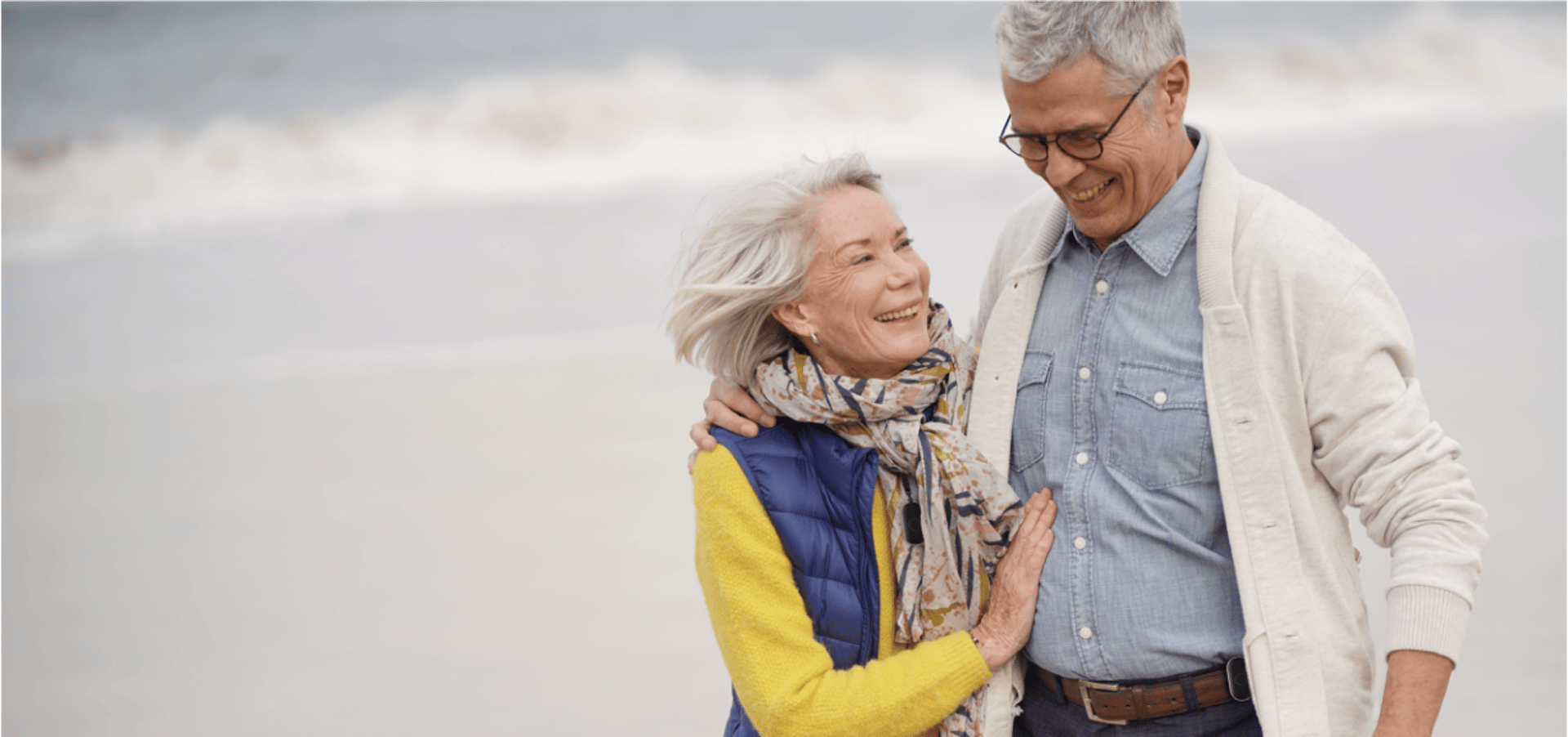 elderly couple in love on a beach, both wearing the pendent. She has it around her neck, he has it clipped to his belt.