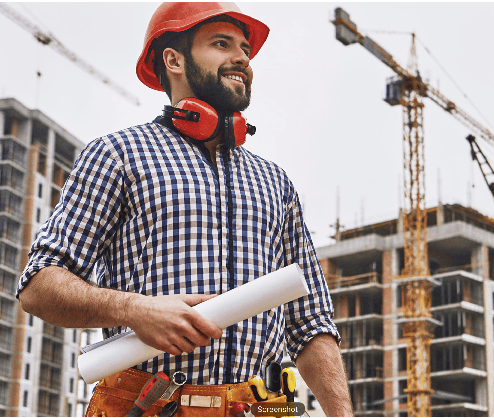 Middle aged man with tool belt, hard hat, paper in hand, and pendent concealed in tool belt. On construction site.