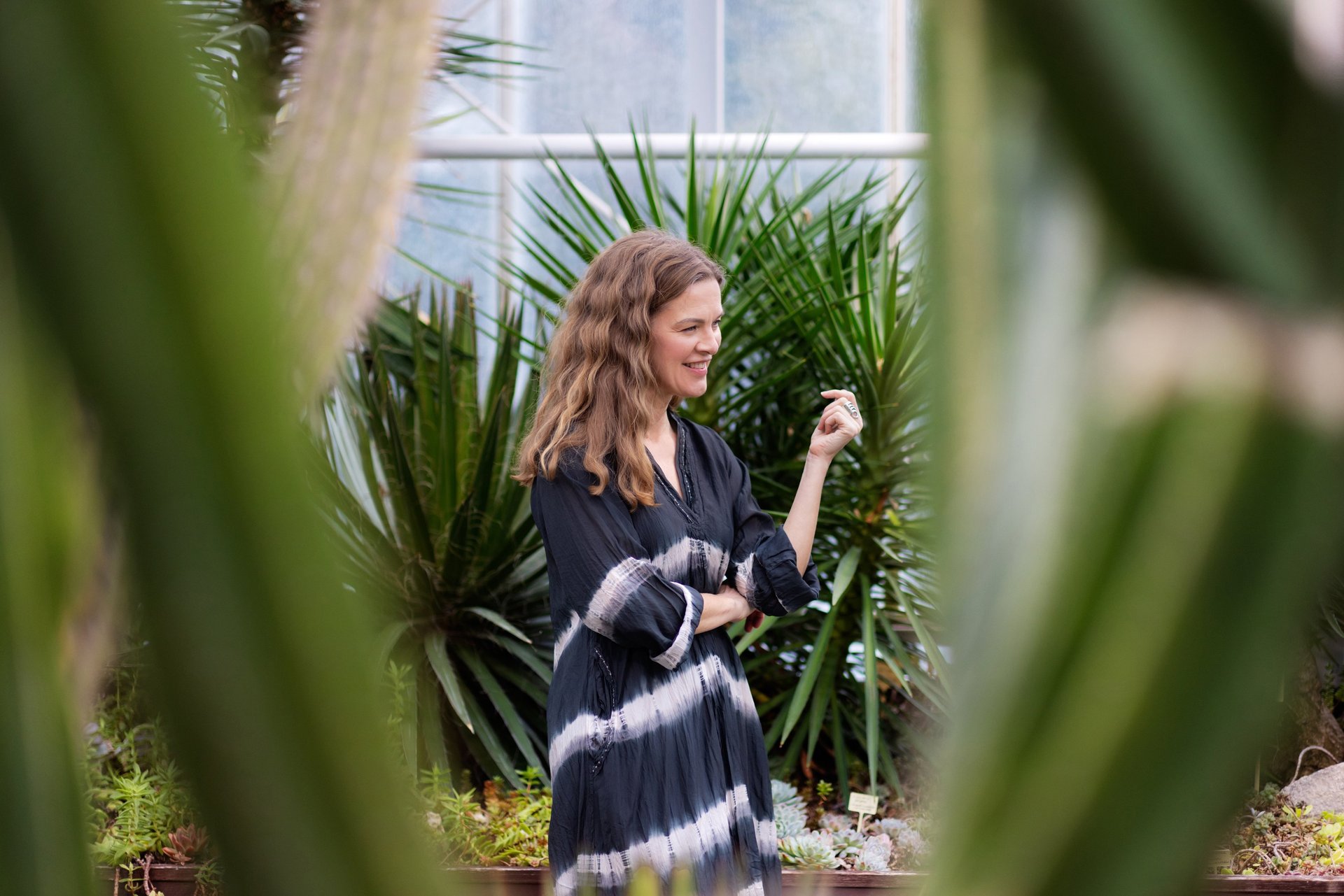 A beautiful middle aged woman with long curly hair standing in a greenhouse