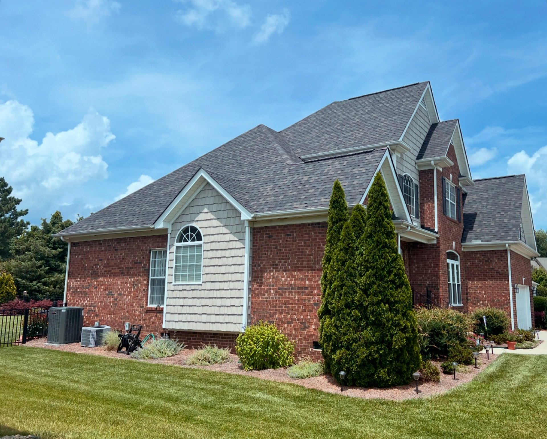 A red brick home with beautiful light gray and tan multicolored shingles. Roof done by Mothership Roofing.