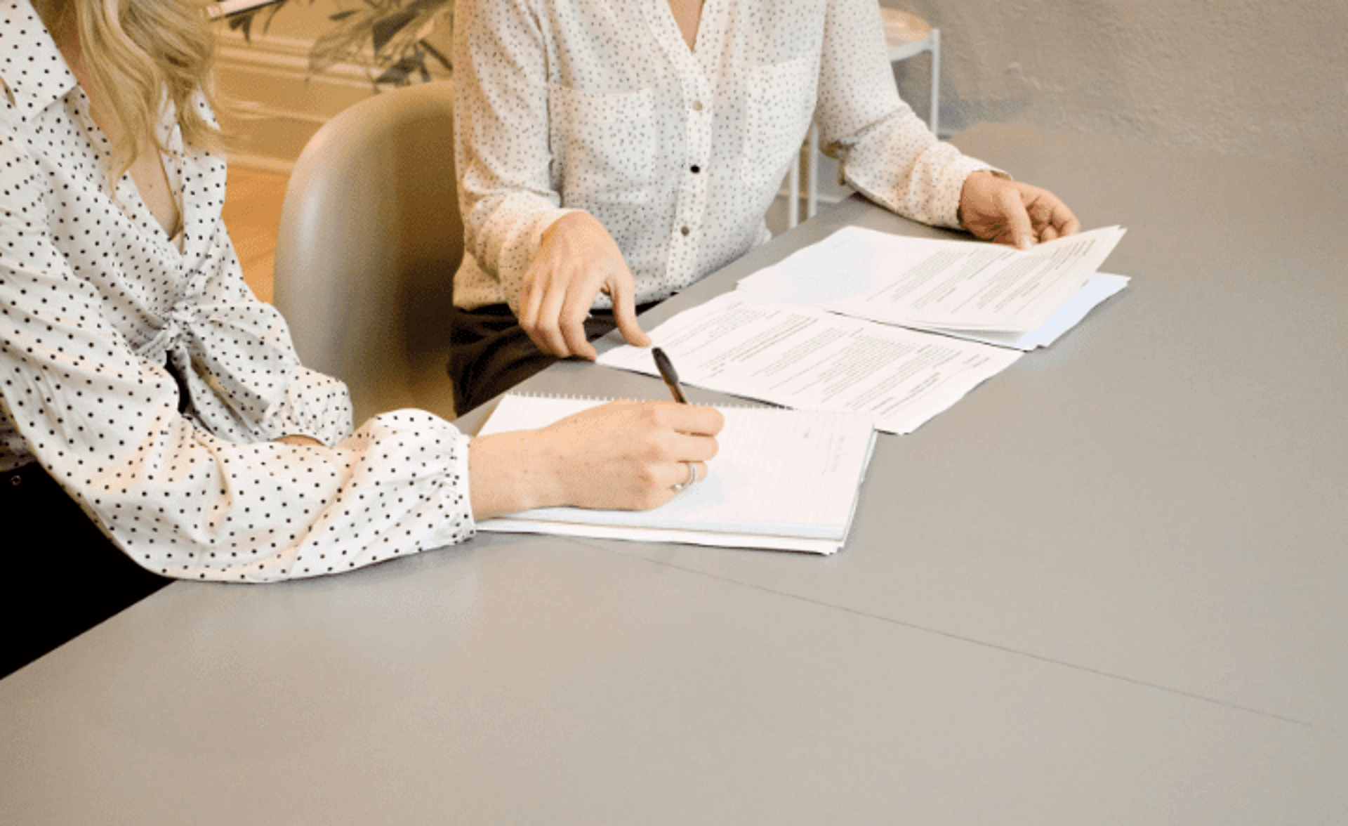 woman signing on white printer paper beside woman about to touch the documents