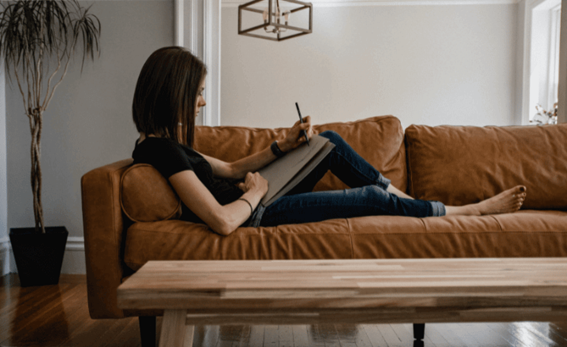 woman in black tank top and blue denim jeans sitting on brown sofa